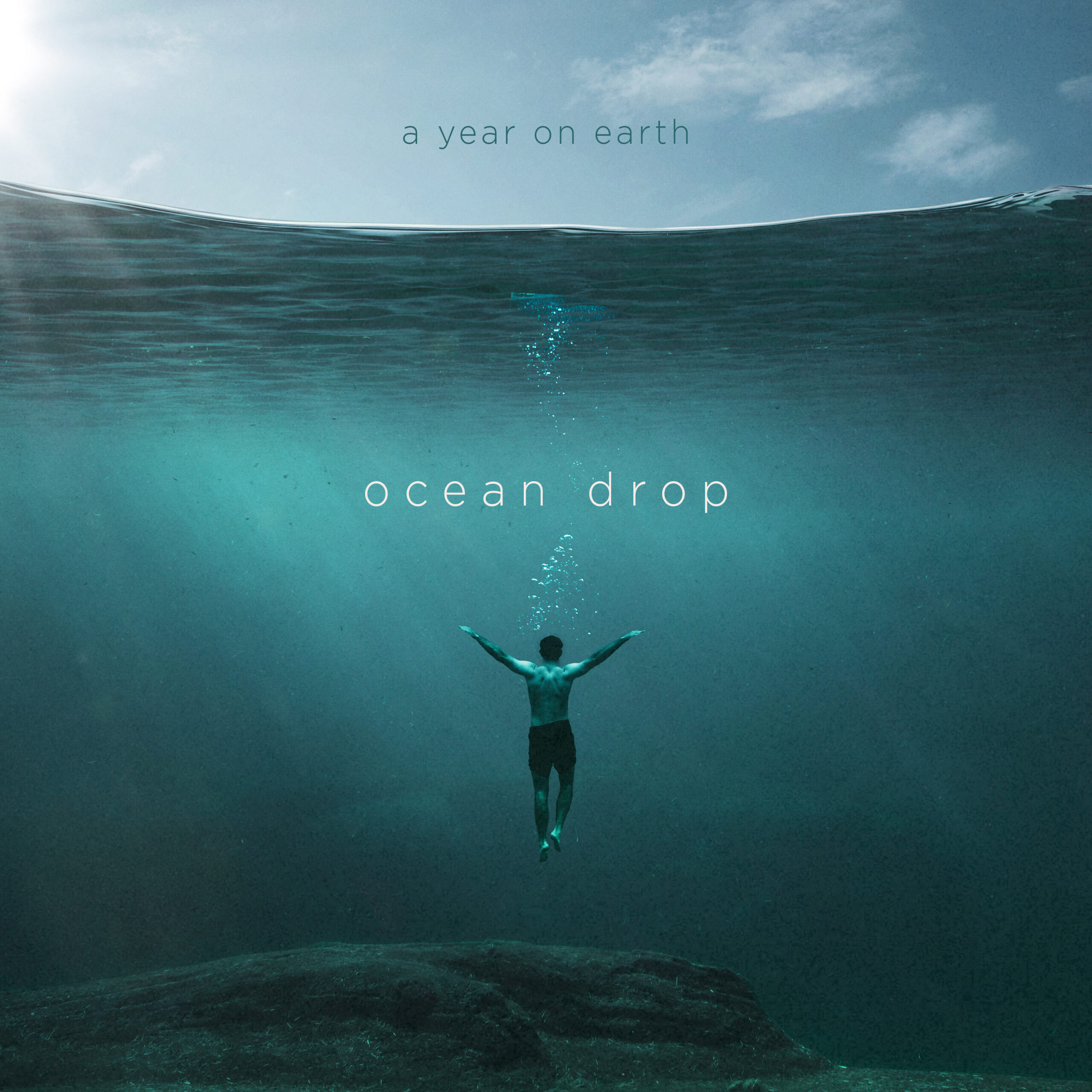 Image of A Year On Earth's "Ocean Drop" Album, released by THHmx. Showing a person floating beneath a calm body of water, with their arms up stretched and a light blue sky above and a greener aquamarine sheen in the water below.